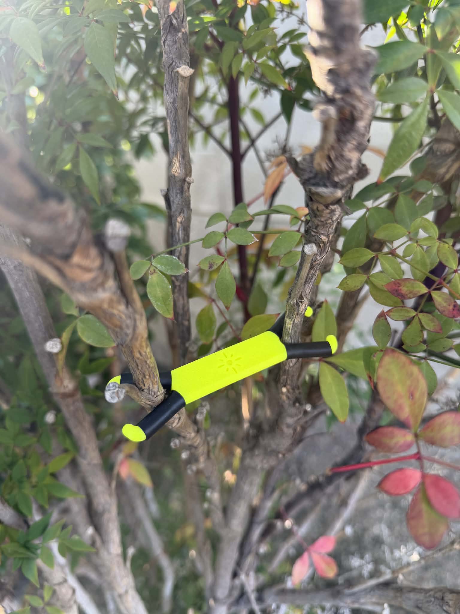 Shine Spine Branch Spreader Photon Burst Yellow 2inch gardening tool attached to a tree branch with green leaves in the background.