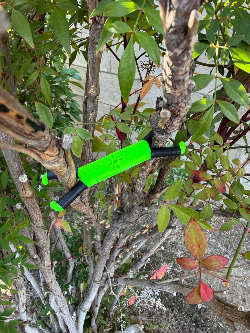 Shine Spine Branch Spreader Radiant Grove Green 2inch gardening tool attached to a tree branch with green leaves in the background.