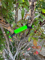 Shine Spine Branch Spreader Radiant Grove Green 2inch gardening tool attached to a tree branch with green leaves in the background.